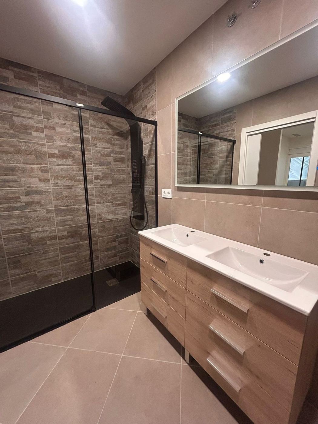 Baño reformado con ducha revestida en piedra y mueble de lavabo doble en madera